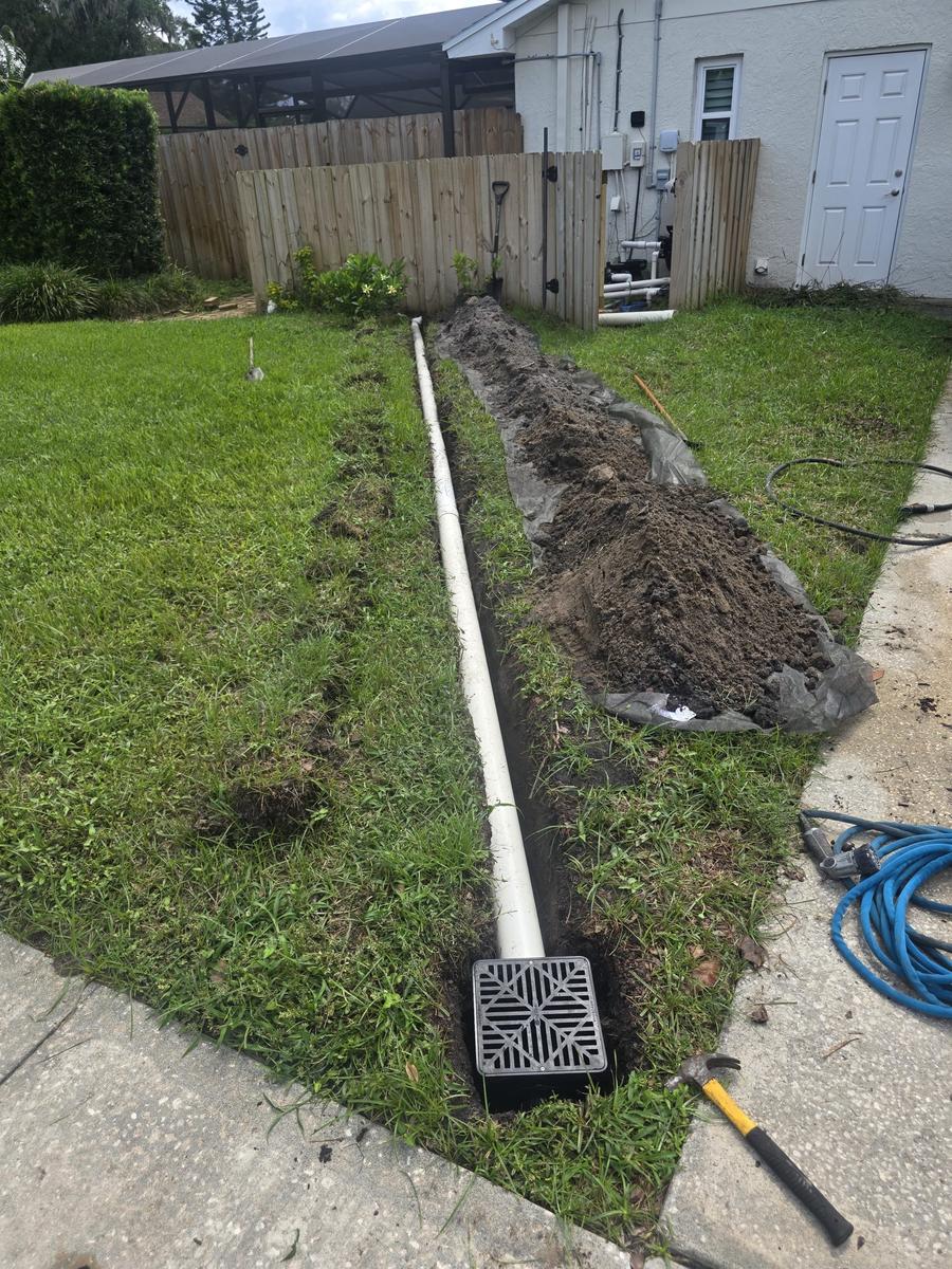 Yard drainage pipe trench running to a catch basin beside a Florida driveway